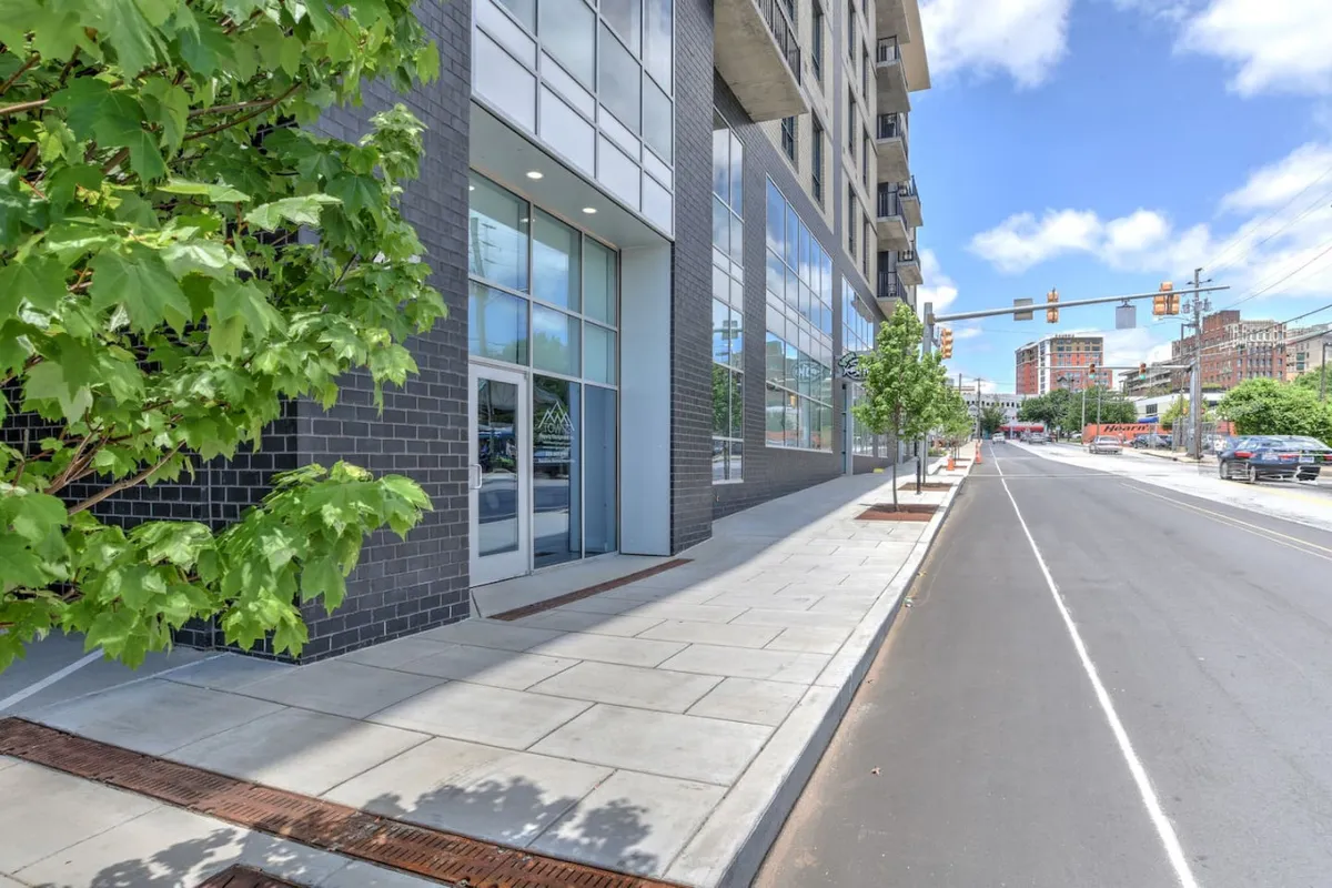 This vibrant street-level view showcases the modern facade of the building, the bustling sidewalk, lush street trees, and city traffic signals, illustrating the convenience of city living and immediate proximity to Asheville’s amenities.