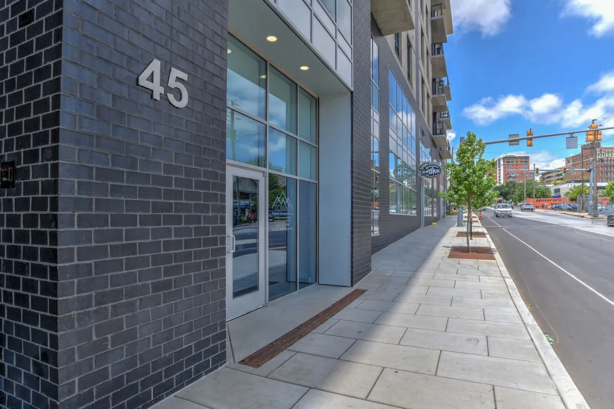 The photo highlights the building's entrance set along a bustling urban street, with clear visibility of the entryway and the street number. Sidewalk activity and nearby shops give a sense of the vibrant, walkable downtown location.