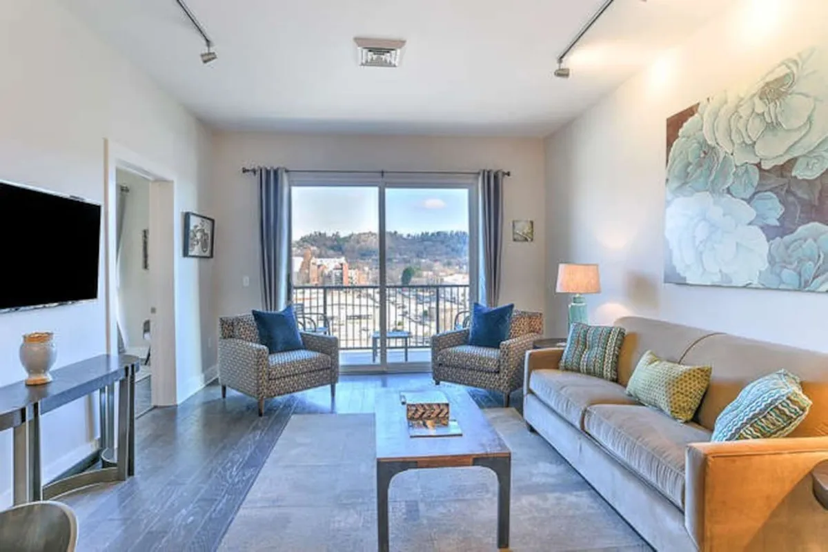 A welcoming living room featuring a comfortable sofa, stylish artwork, and a large window framing a city view. Natural light fills the space, creating an inviting atmosphere for relaxation or socializing. The modern decor and plush seating set the stage for cozy gatherings, game nights, or quiet afternoons.