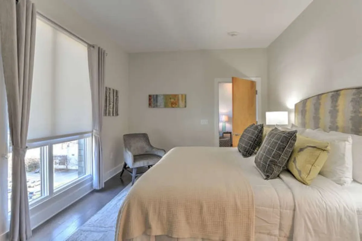 This image features another tranquil bedroom with a beautifully made bed, an armchair perfect for reading or morning coffee, and eye-catching wall art. The space is bathed in natural light, emphasizing the condo’s relaxing atmosphere and suitability for both work and relaxation.